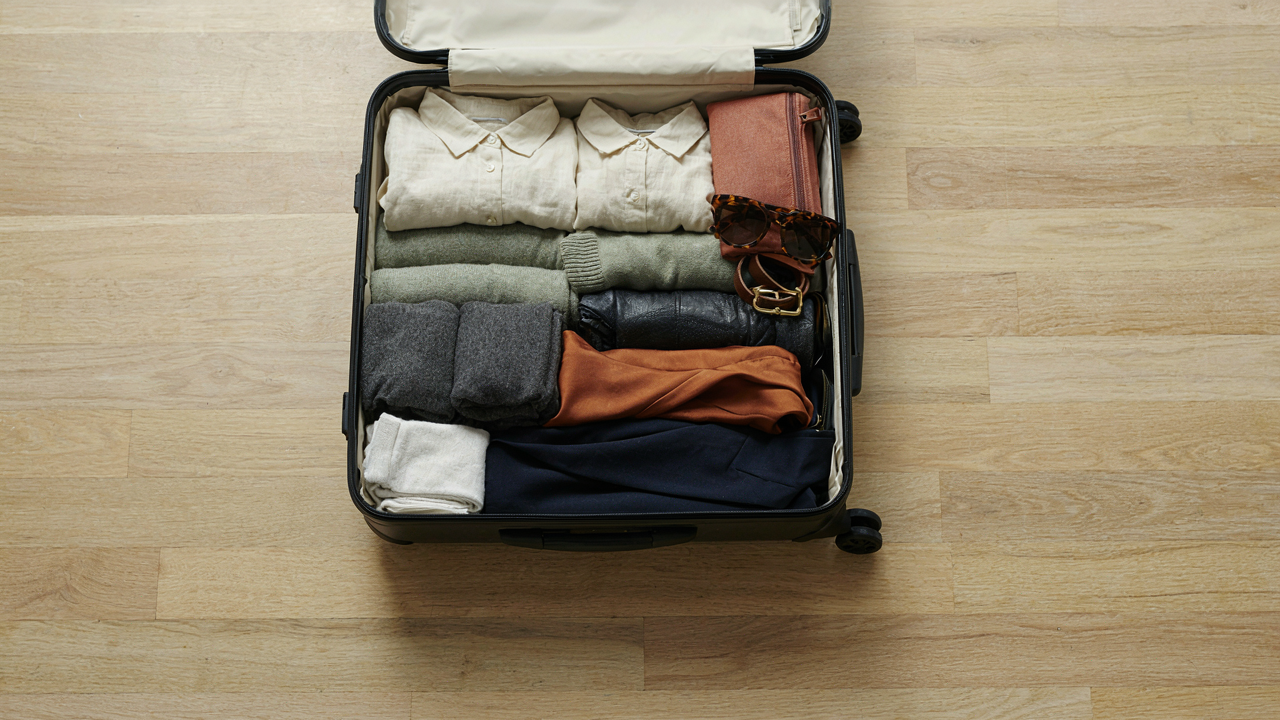 An open suitcase filled with a neatly organized 3 week travel capsule wardrobe.