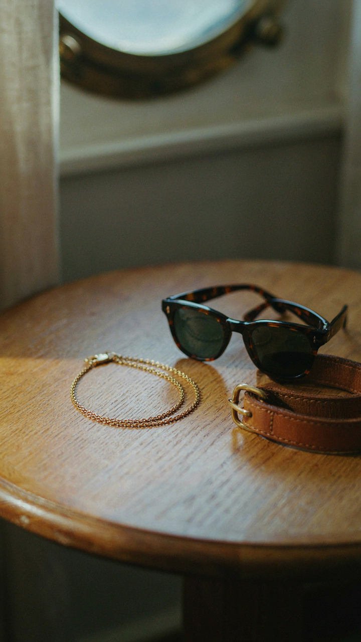 A gold necklace, sunglasses, and a fabric belt are on a cabin table.