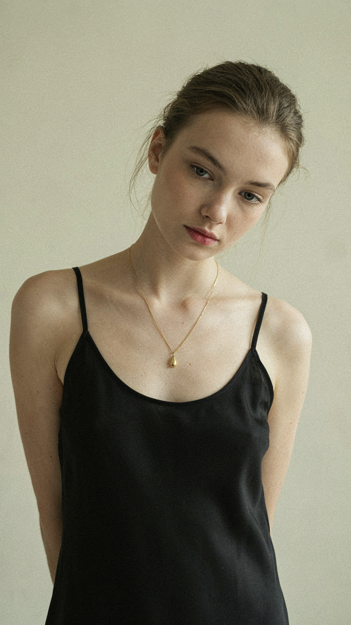 A single gold pendant necklace rests on a black dress.