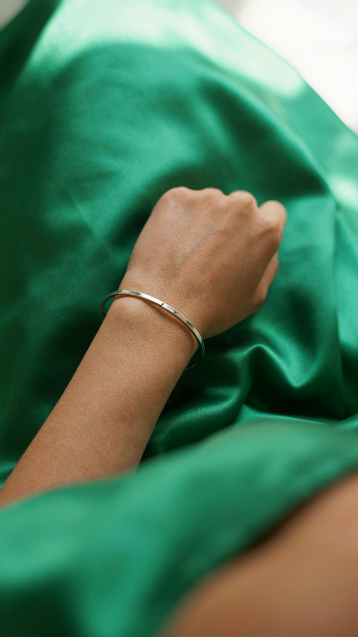 Close-up of an elegant silver bracelet against an emerald green satin dress.