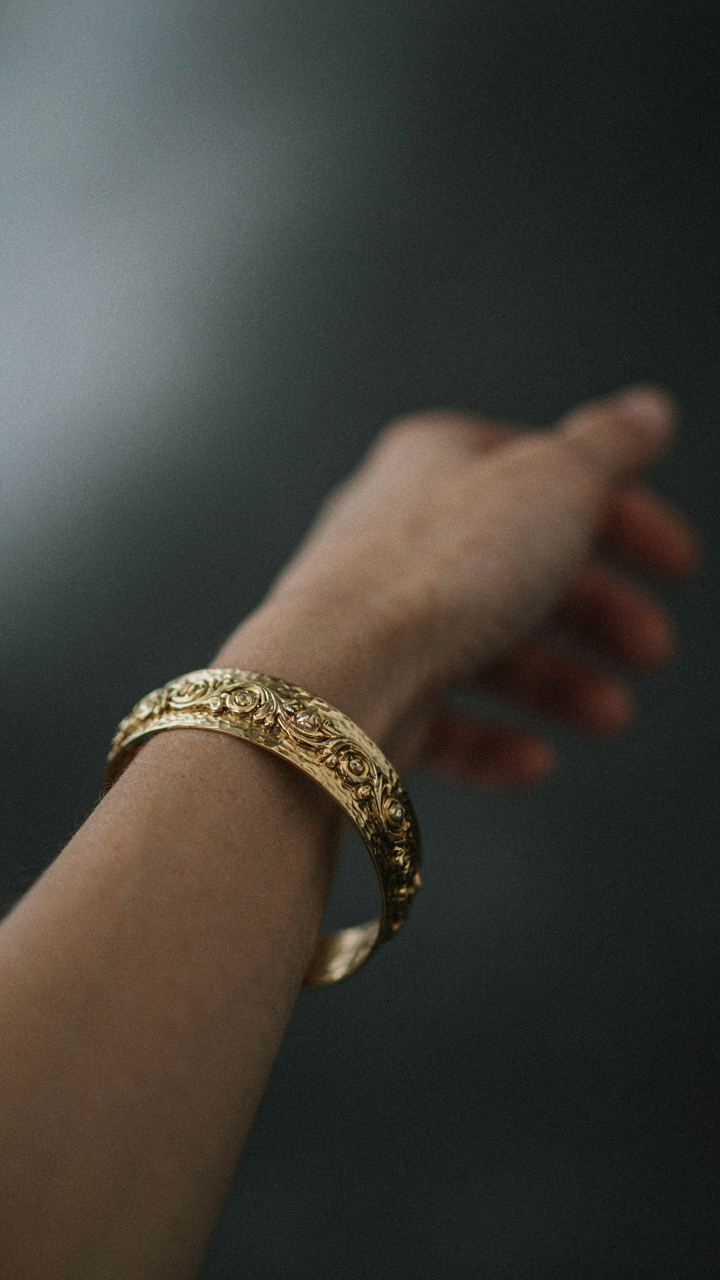 A gold cuff bracelet sparkles on a woman's wrist in dim light.
