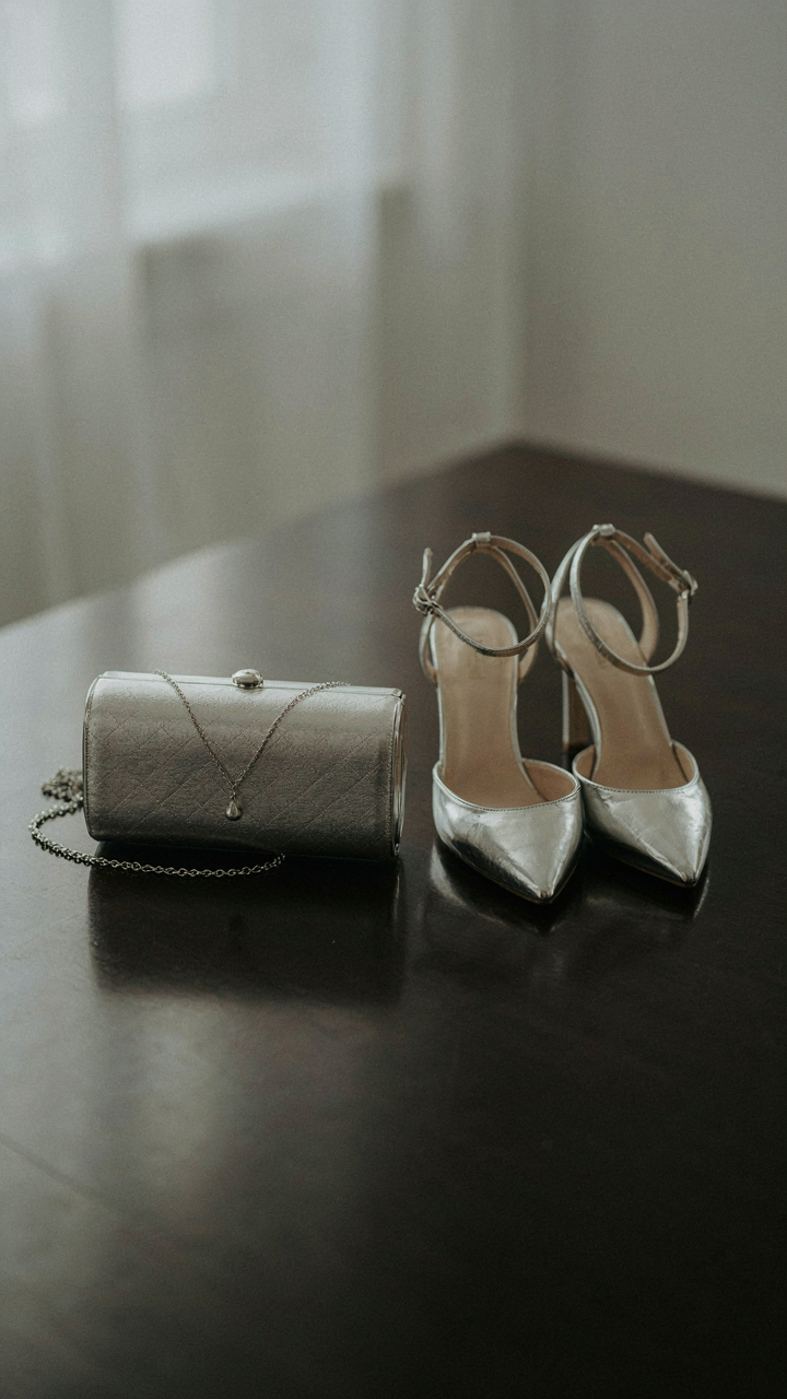 An elegant silver clutch, strappy silver heels, and a silver necklace.