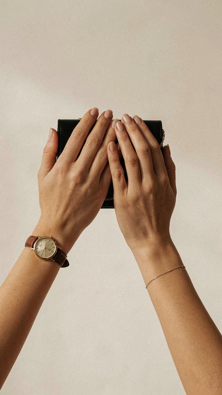 A hand wears an elegant watch and holds a clutch bag.