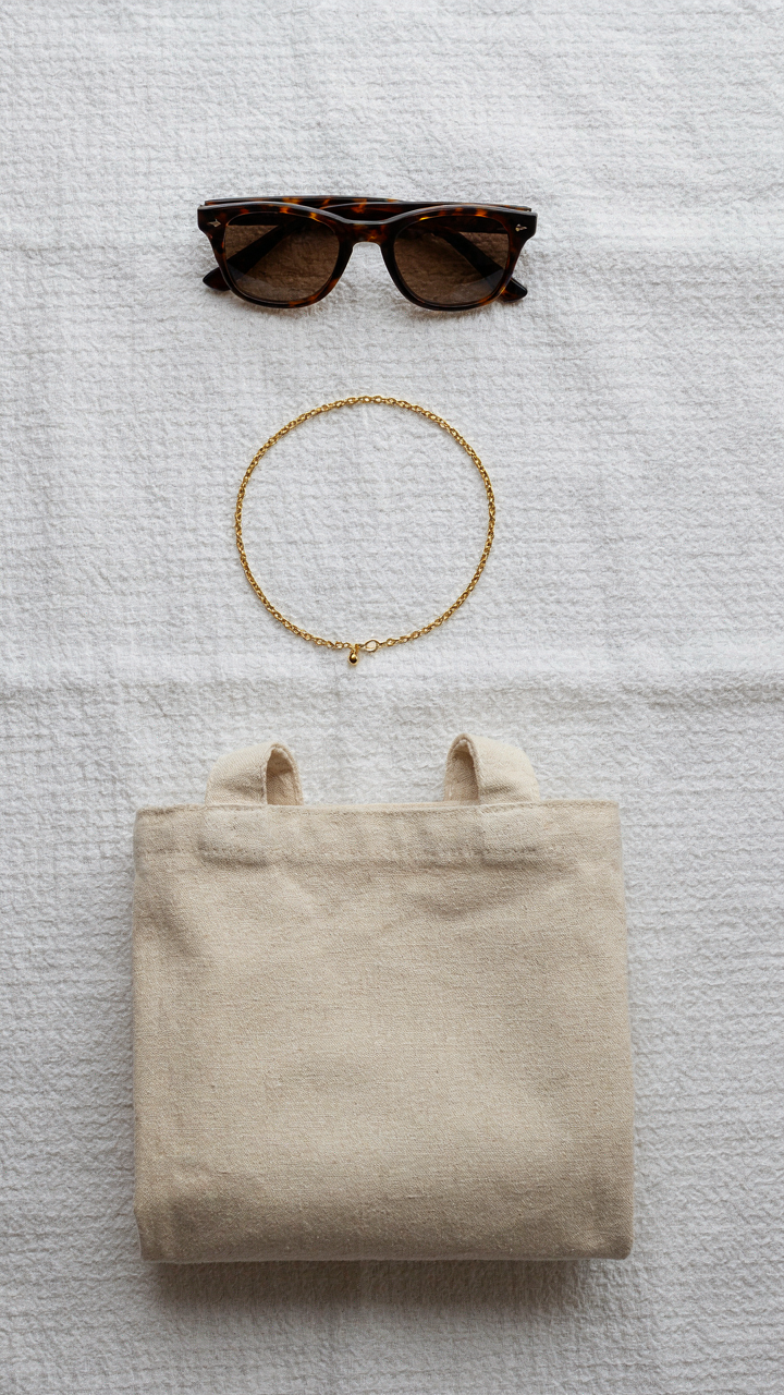 A gold chain necklace, sunglasses, and a neutral canvas tote bag.