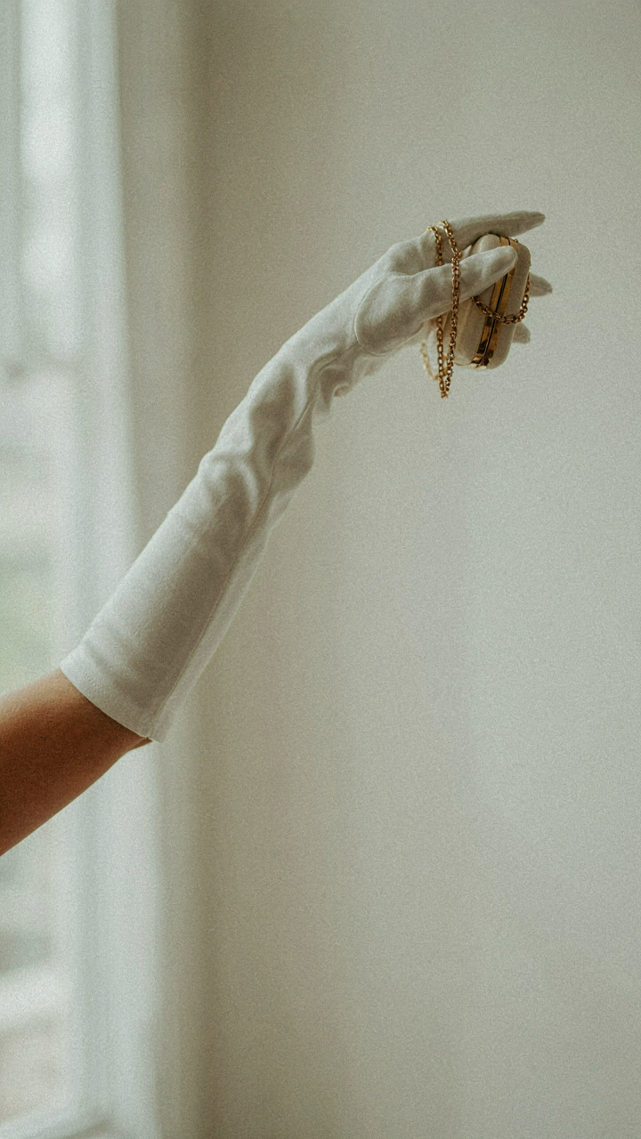 A woman's arm with a long white opera glove holds a clutch bag.