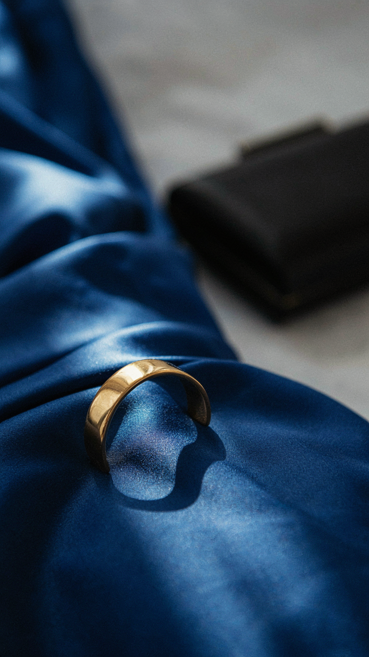 A gold cuff bracelet rests on a royal blue satin jumpsuit with a black clutch.