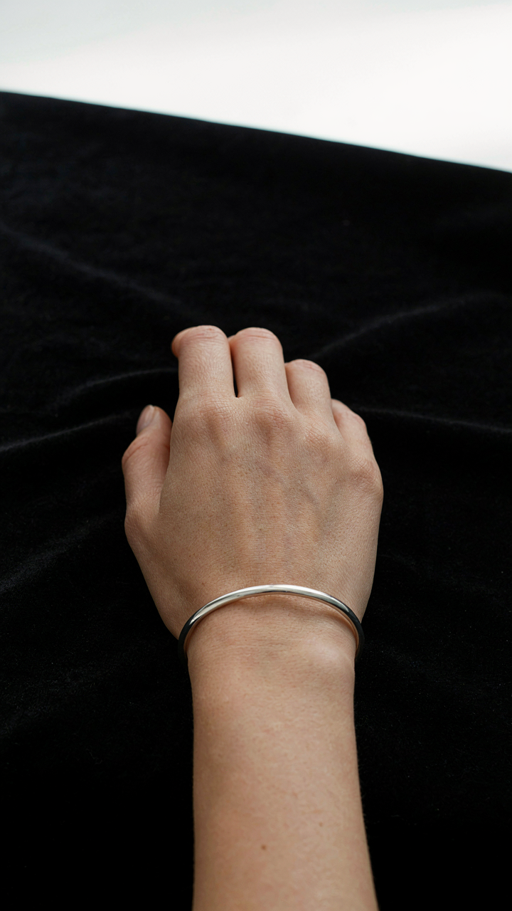 A woman's hand holds a shiny silver bracelet on black velvet.