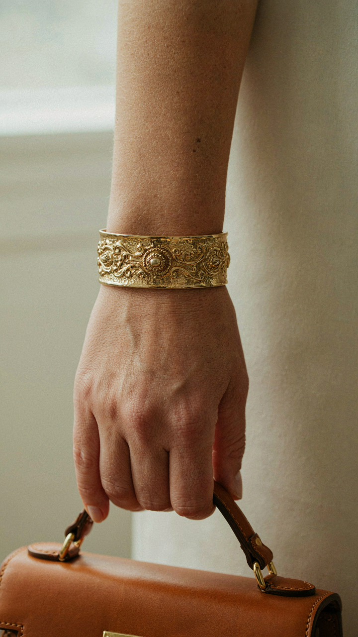 A wrist with a substantial cuff bracelet holds a structured handbag.