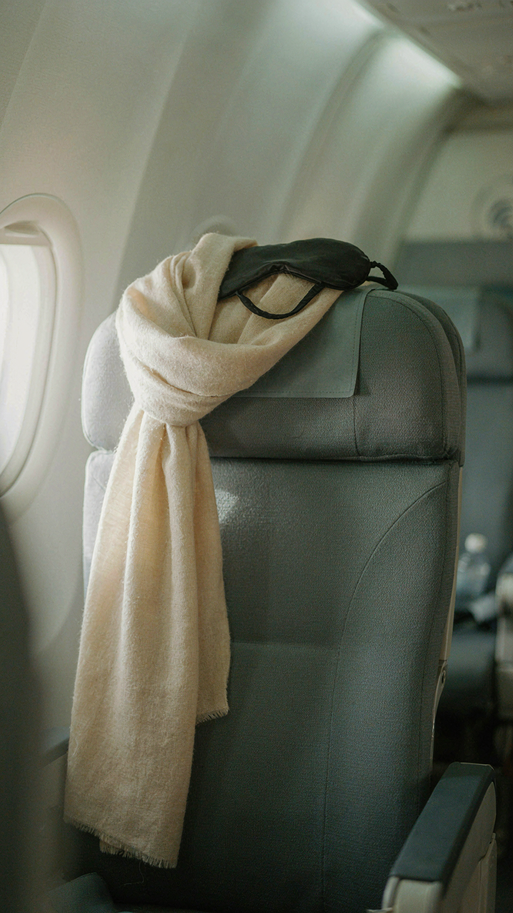 Soft scarf draped over an airplane seat with an eye mask on the headrest.