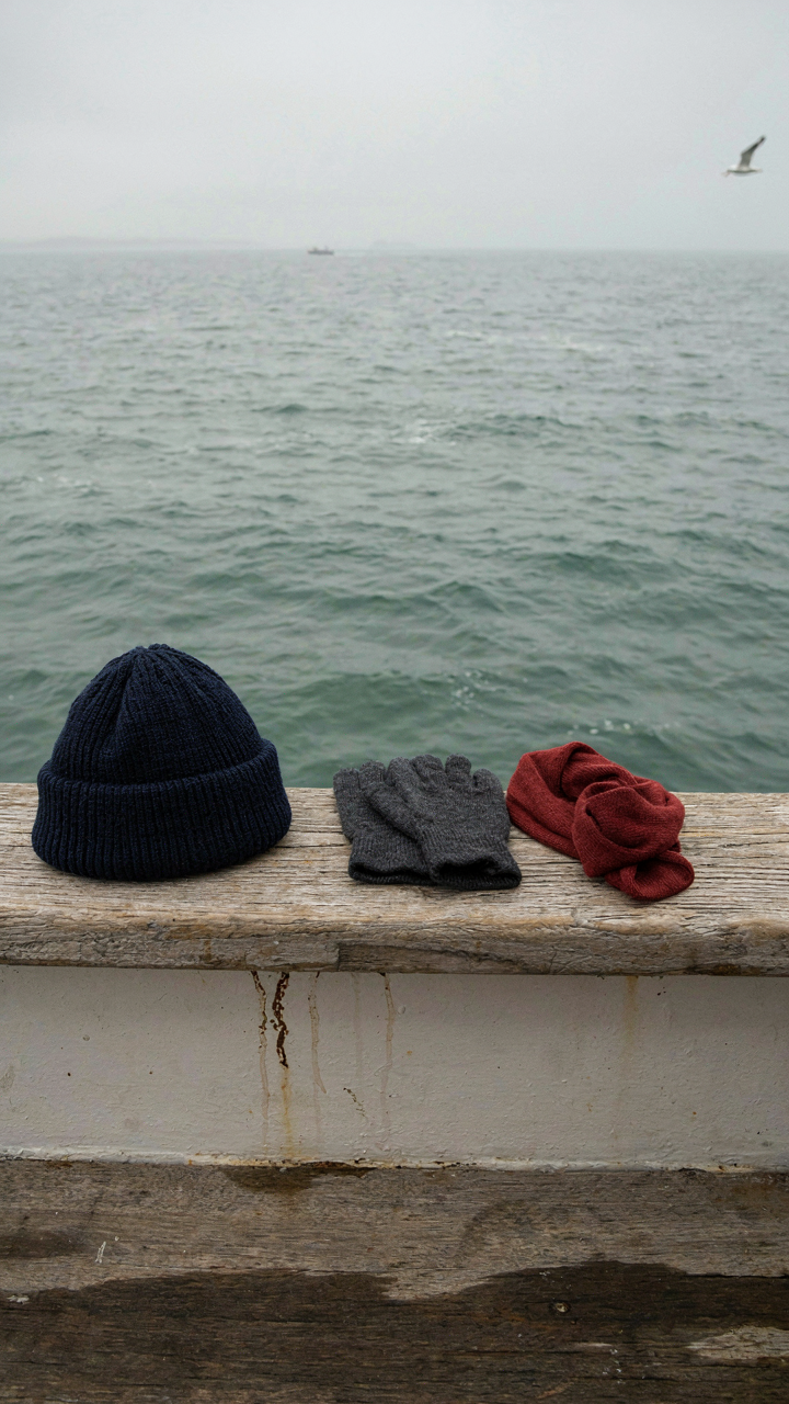 A wool beanie, merino gloves, and a neck gaiter on a ship railing.
