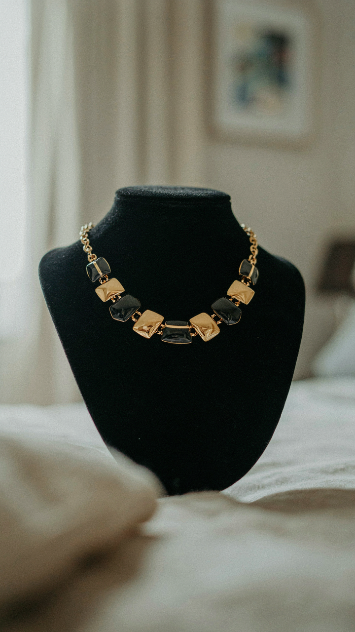 A single bold geometric statement necklace on a black velvet stand in a hotel room.
