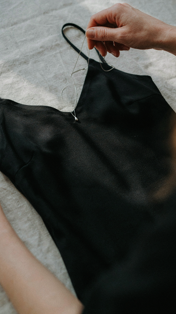 A woman places a simple silver necklace over a black office christmas party dress.