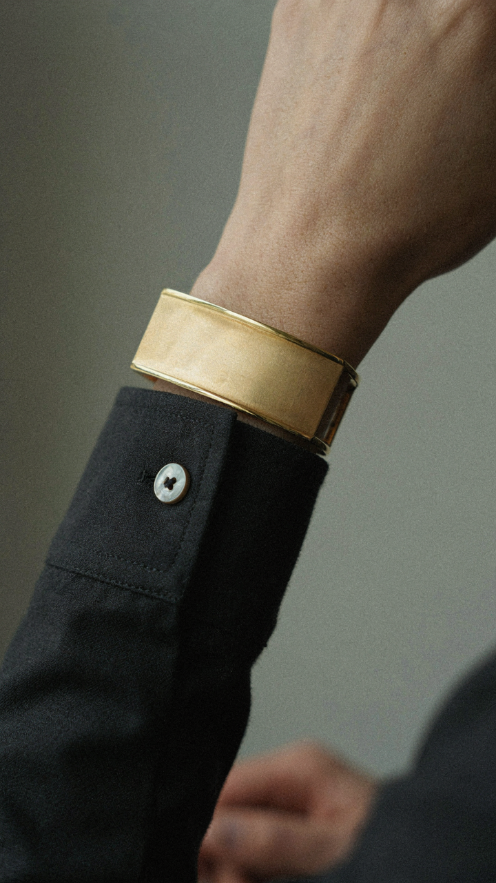 A single gold cuff bracelet on the wrist of a tailored long sleeve.