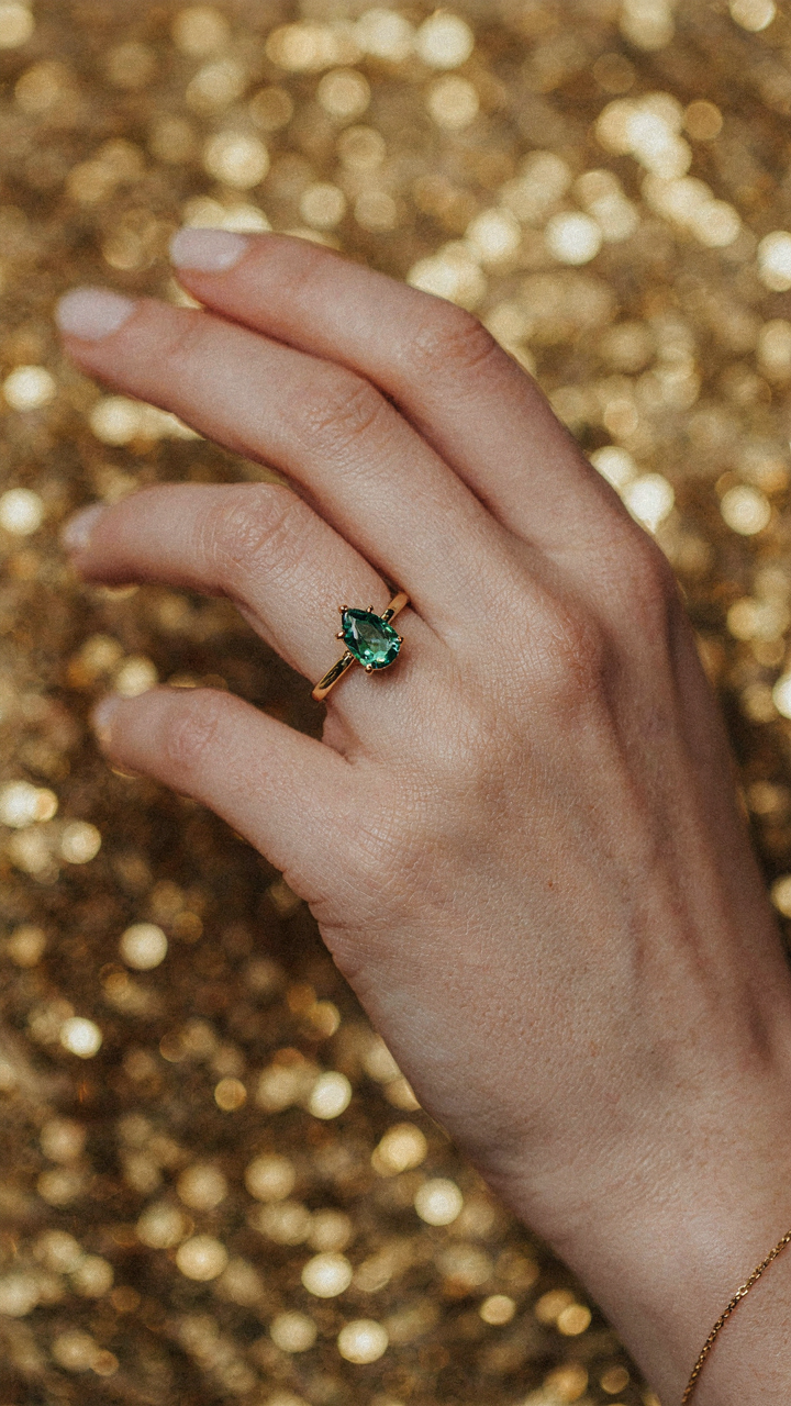An elegant cocktail ring with golden sequins blurred in the background.