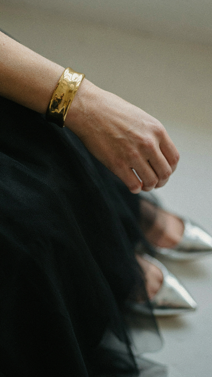A chunky gold cuff bracelet is visible next to a black tulle skirt.