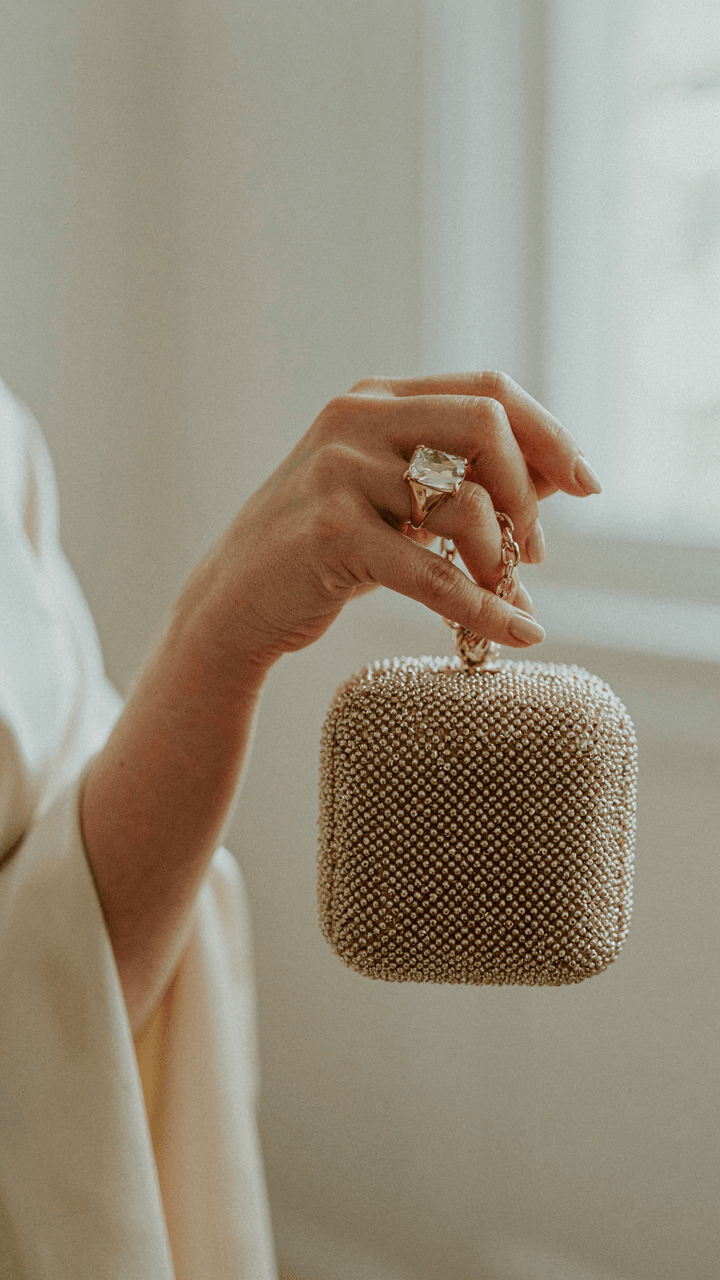 Hand with a cocktail ring holding a beaded clutch, partially covered by a wrap.