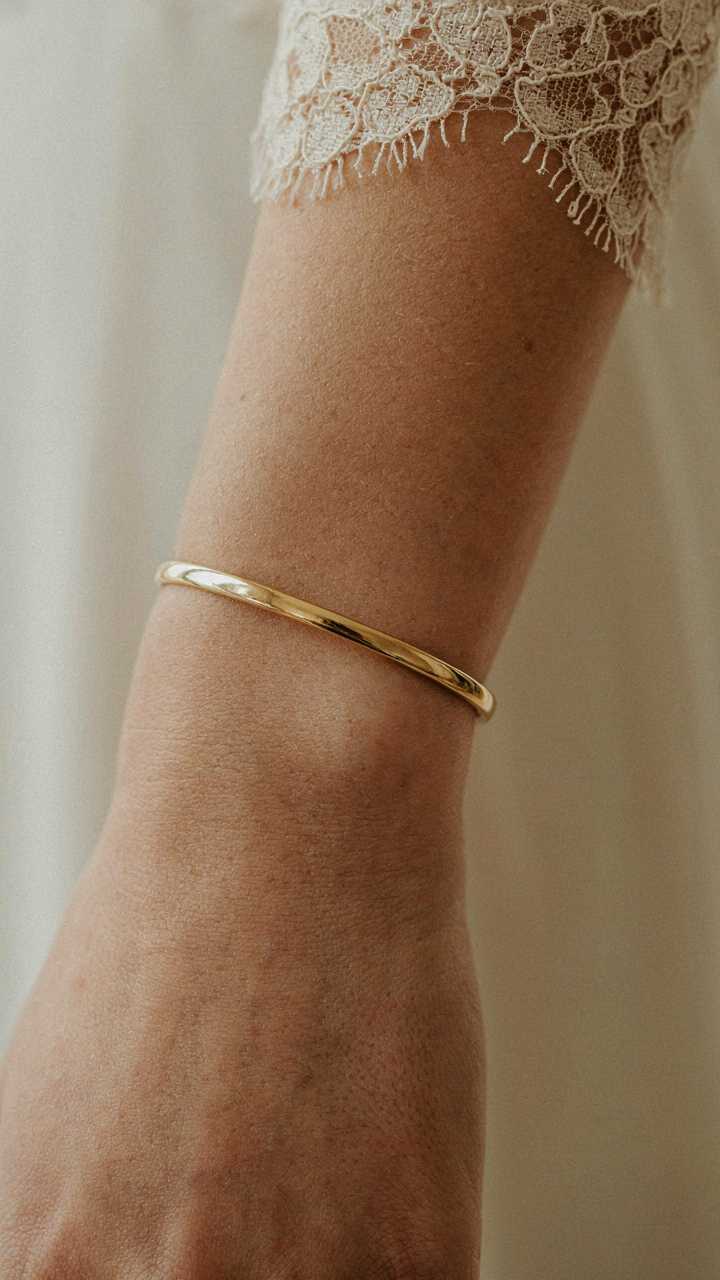 A striking gold cuff bracelet on a woman's wrist against a lace dress.