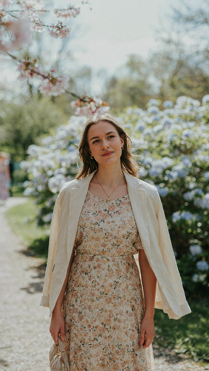 A woman in a layered floral dress and light jacket on a breezy spring day.