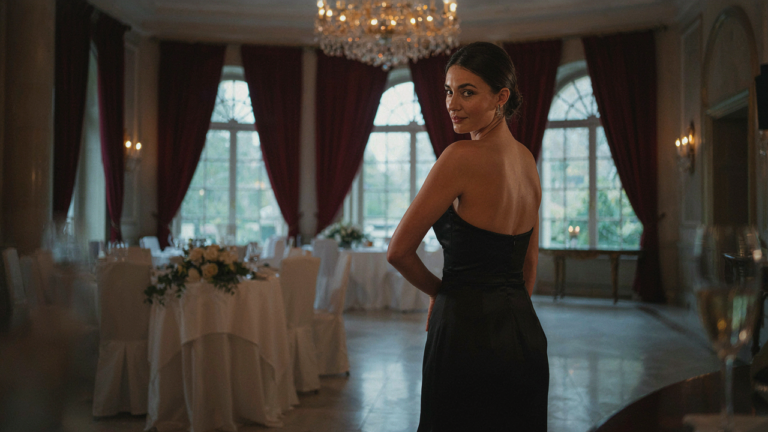 Woman in a black backless cocktail dress poses in a luxurious hotel ballroom.