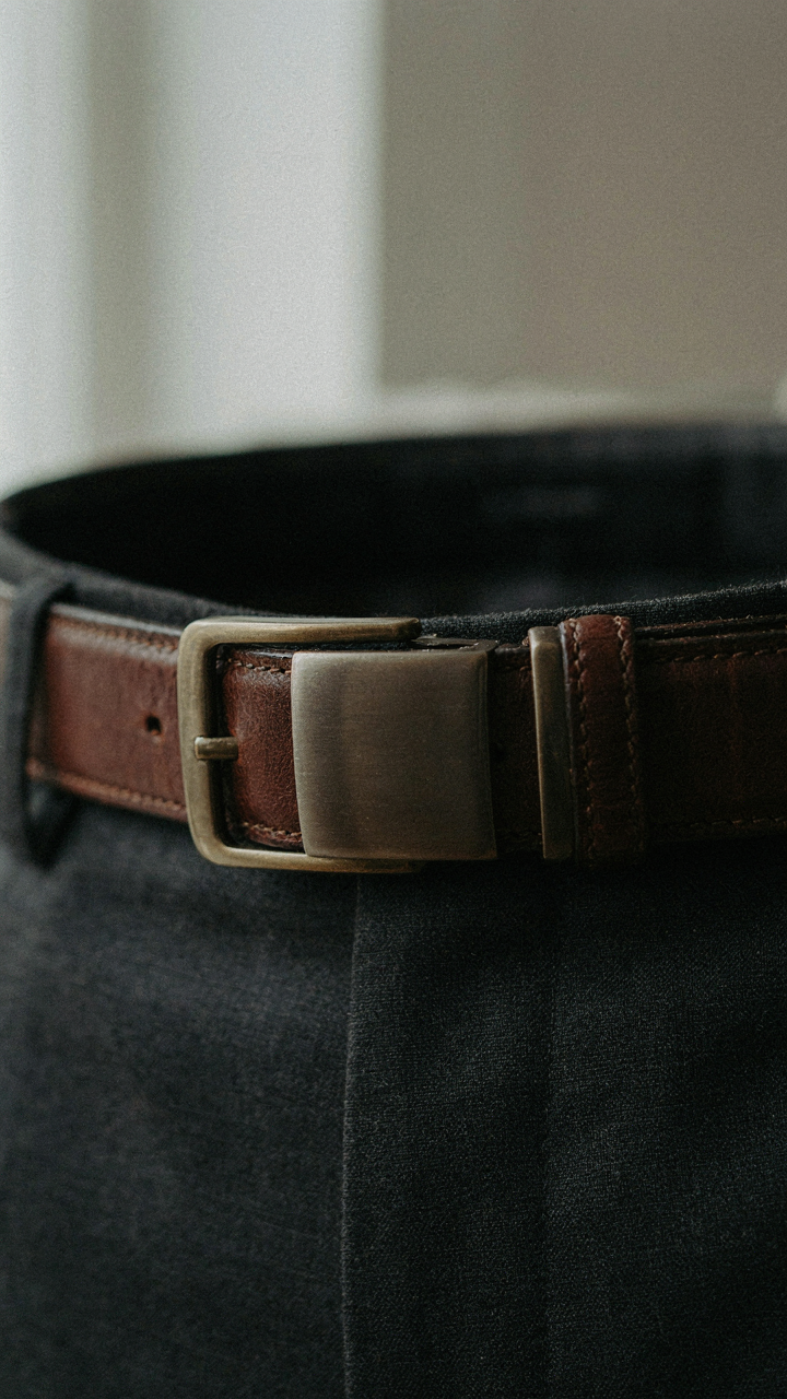A dark leather belt with a simple brushed gunmetal buckle is worn with a suit.
