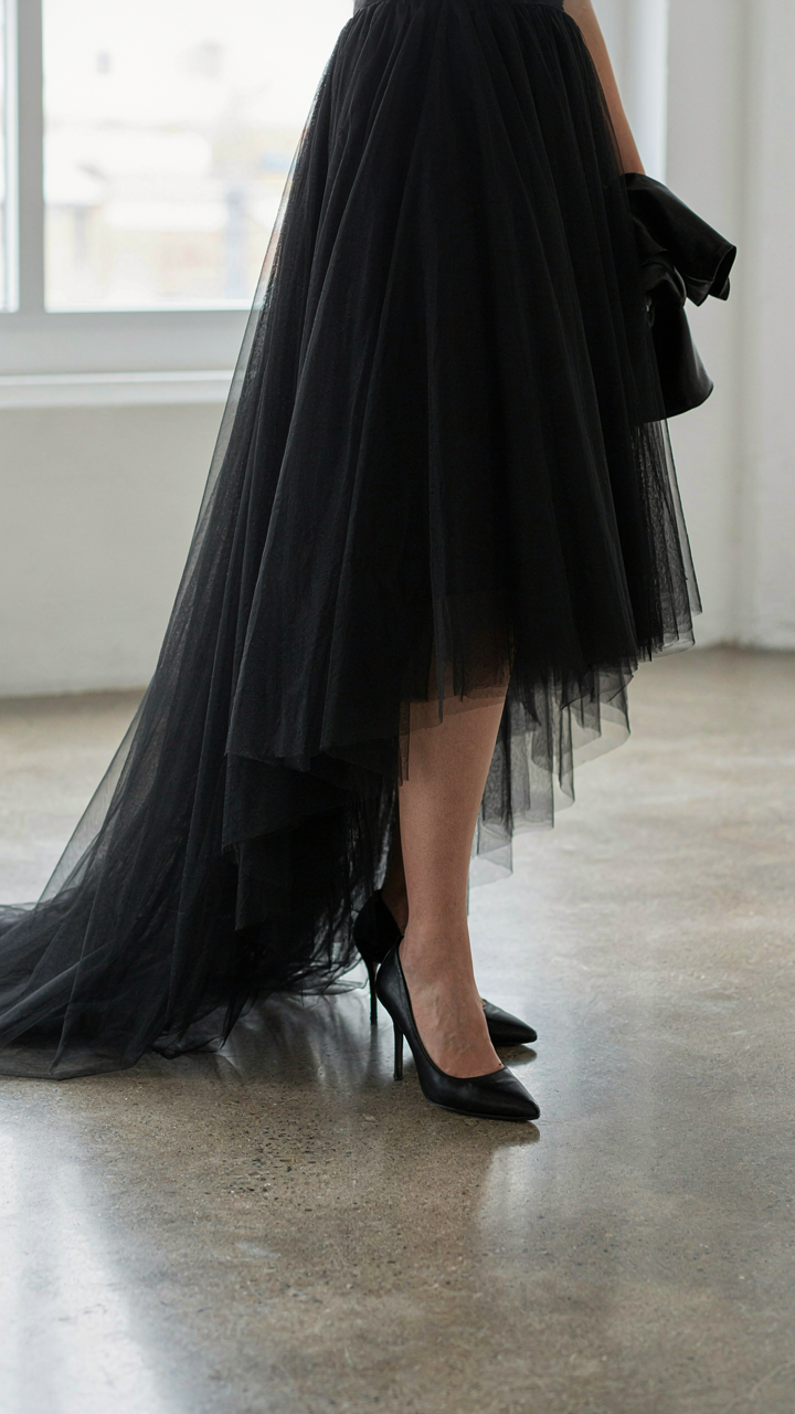 A woman's black high-low tulle skirt and pointed shoes with a leather jacket.