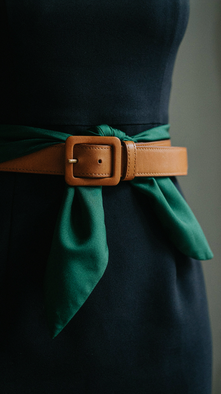 An emerald silk scarf is draped over a structured belt on a navy dress.