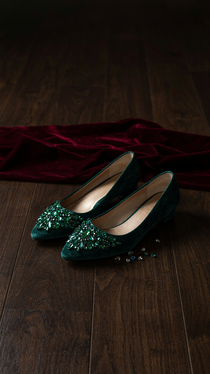 Embellished jewel-toned velvet flats on a dark surface.