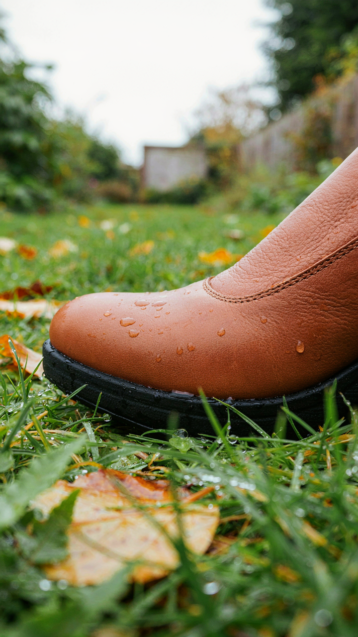 A close-up of a stylish wedge shoe with a sealed leather upper on damp grass.