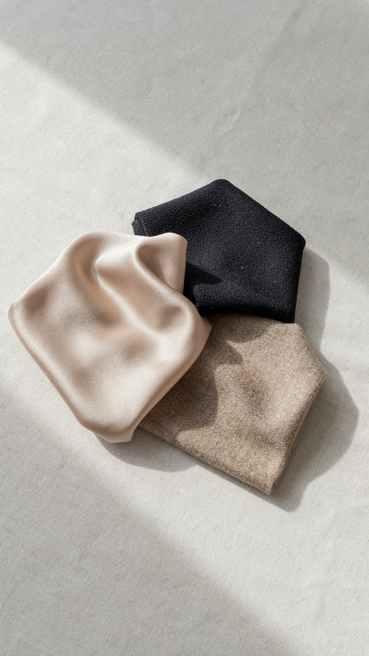 Glossy champagne satin fabric next to matte charcoal crepe and textured wool.
