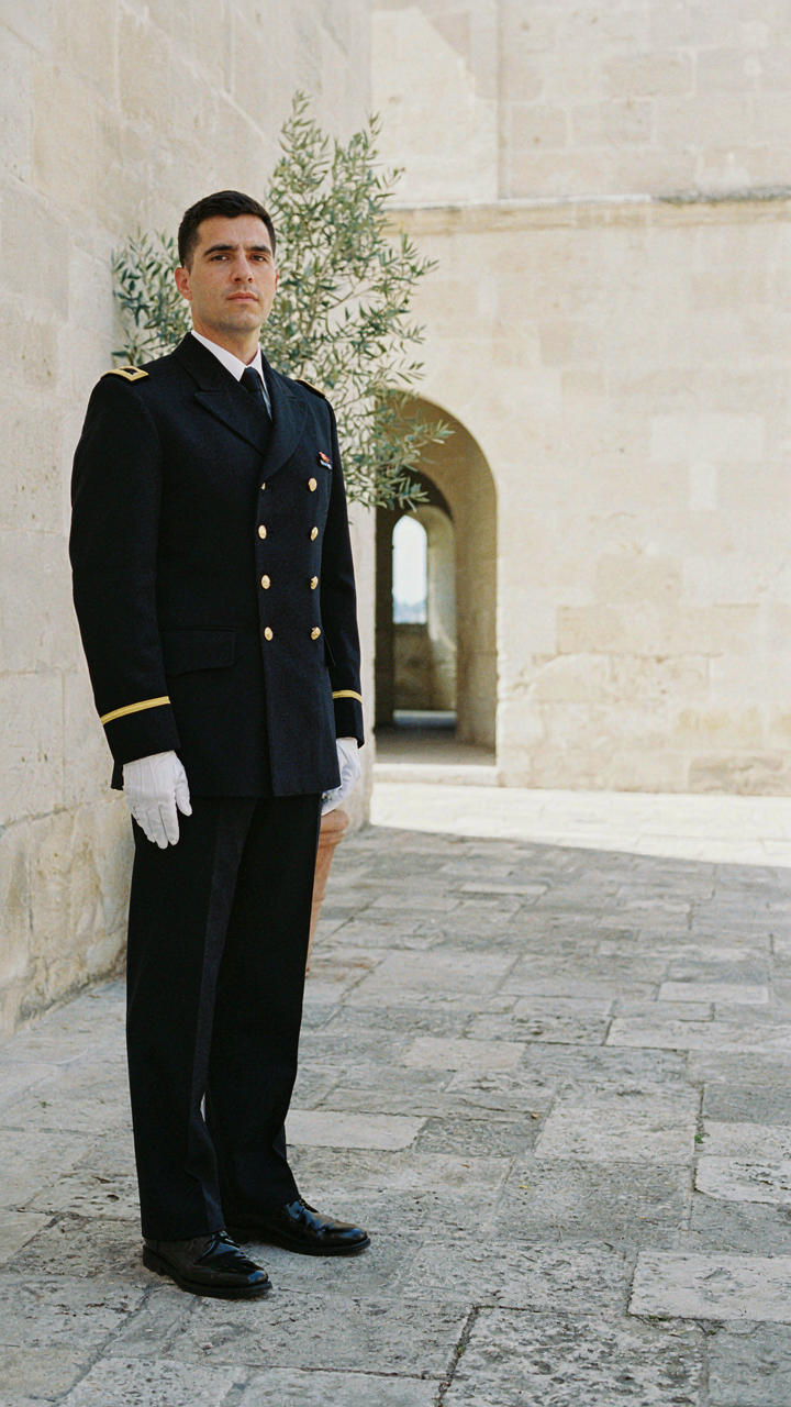 Military officer in a dress uniform stands at attention, showing tailored shoulders.