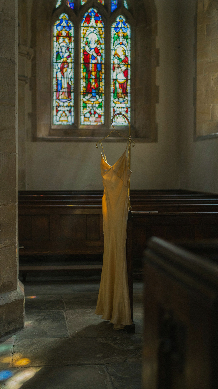 A butter yellow christening guest dress hangs in a sunbeam inside a church.