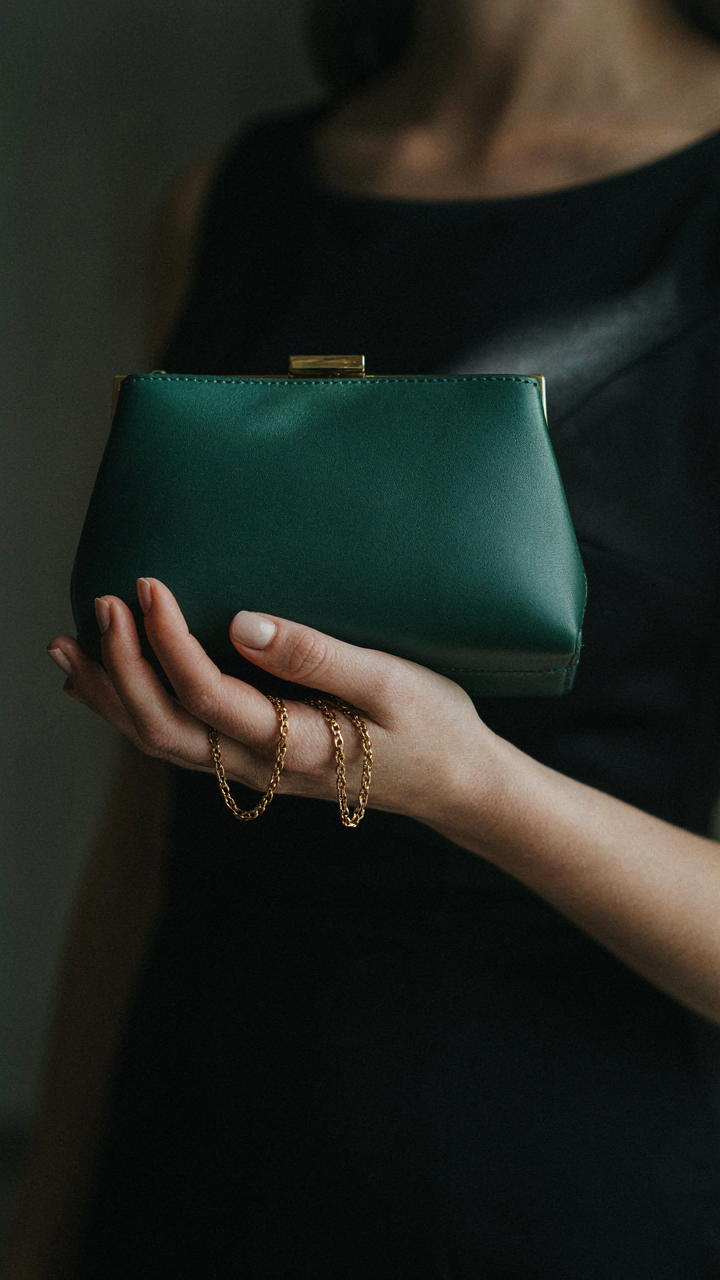 A woman holds an emerald green handbag against a black dress.