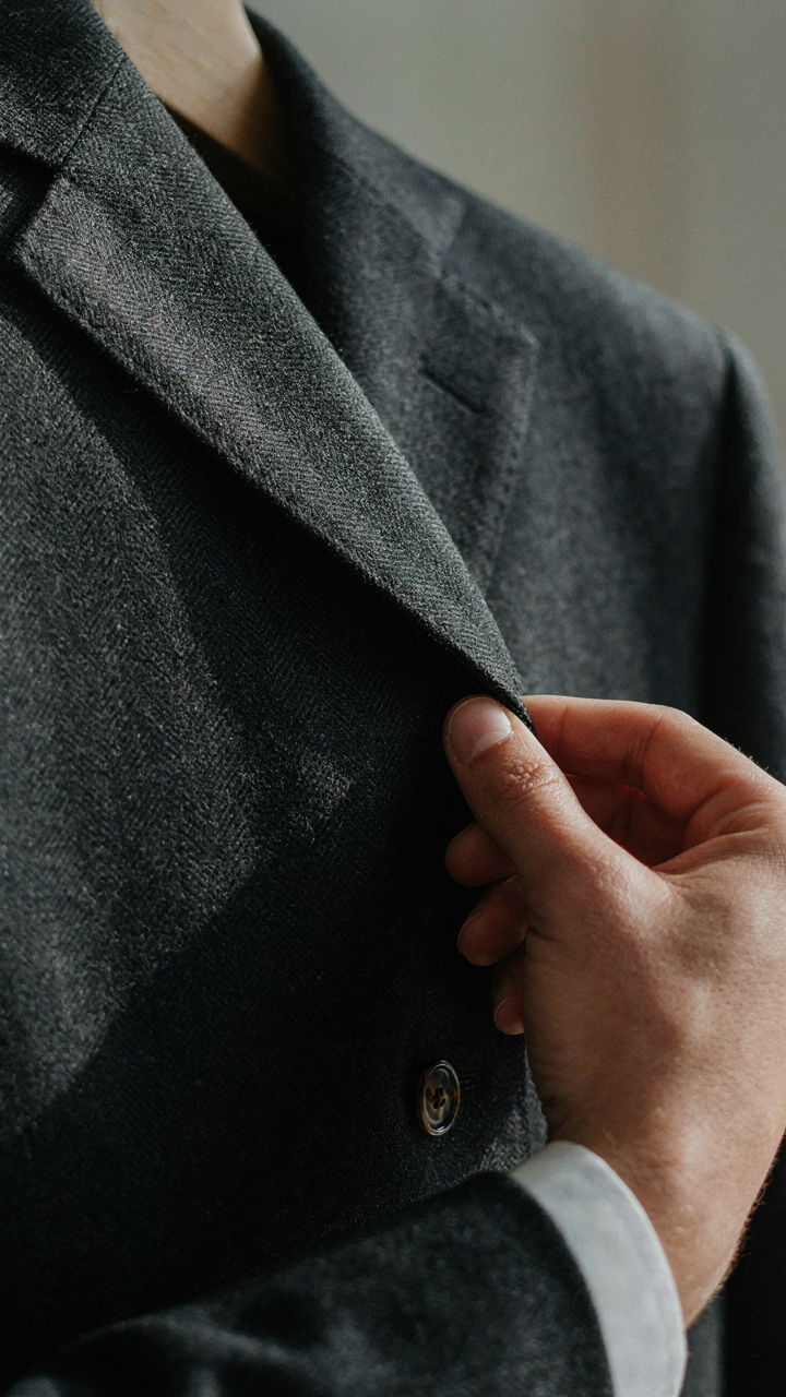 A hand inspecting the high-quality fabric of a dark blazer.