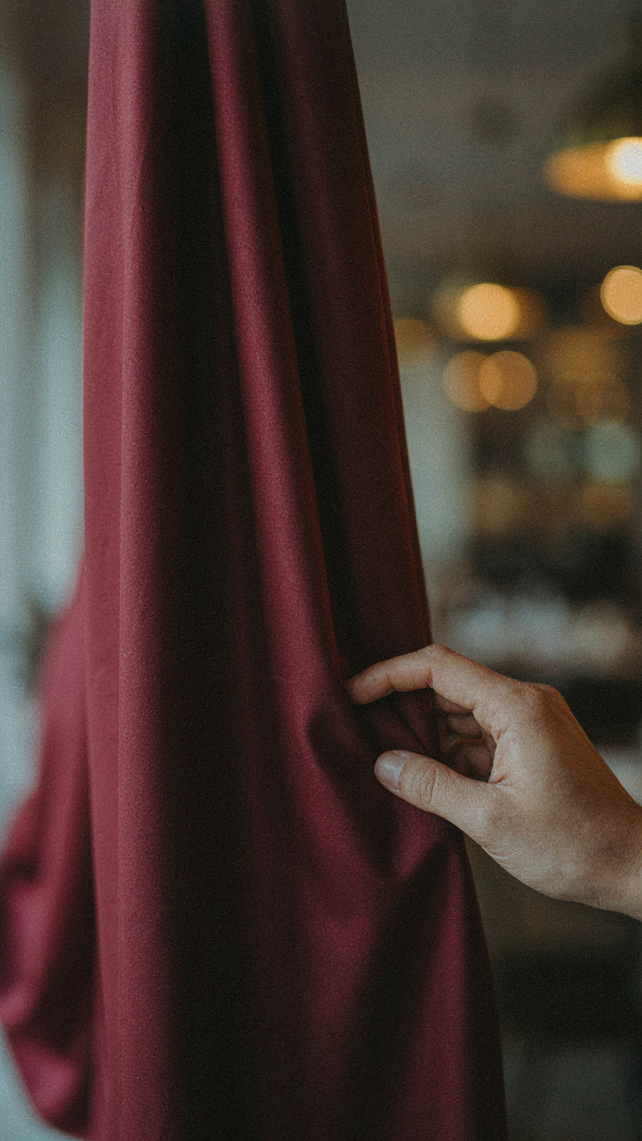 A close-up of a hand touching luxurious burgundy silk fabric.