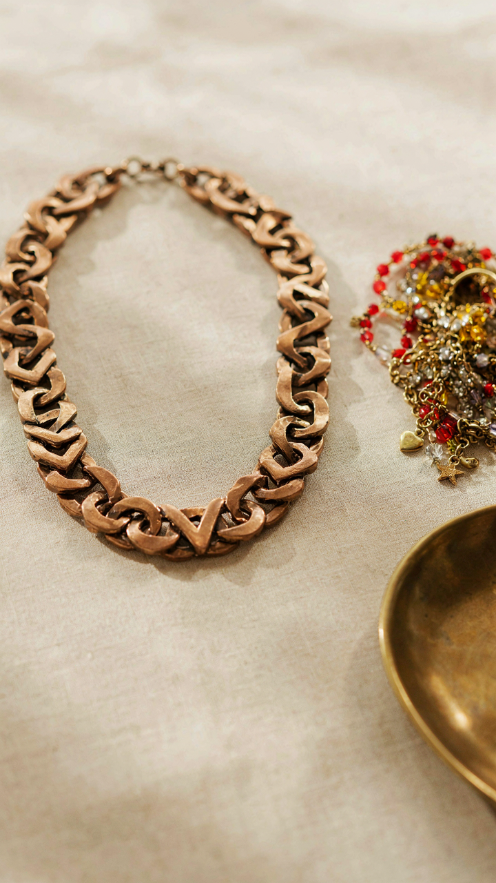 A bronze statement necklace is displayed next to a cluttered costume necklace.
