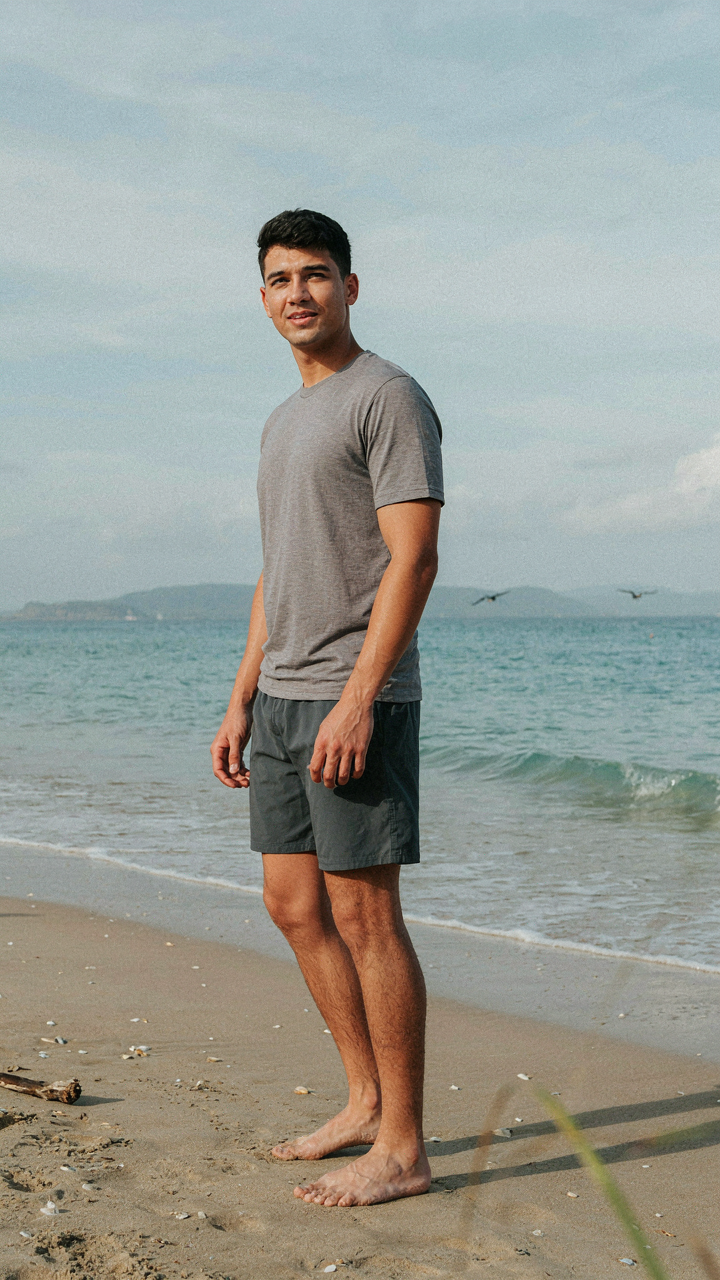 A person in simple, functional swim shorts and a t-shirt on a beach.