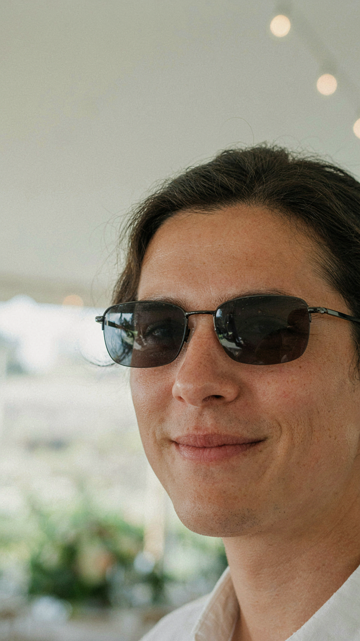 A person's face looks relaxed behind polarized sunglasses at an outdoor wedding.