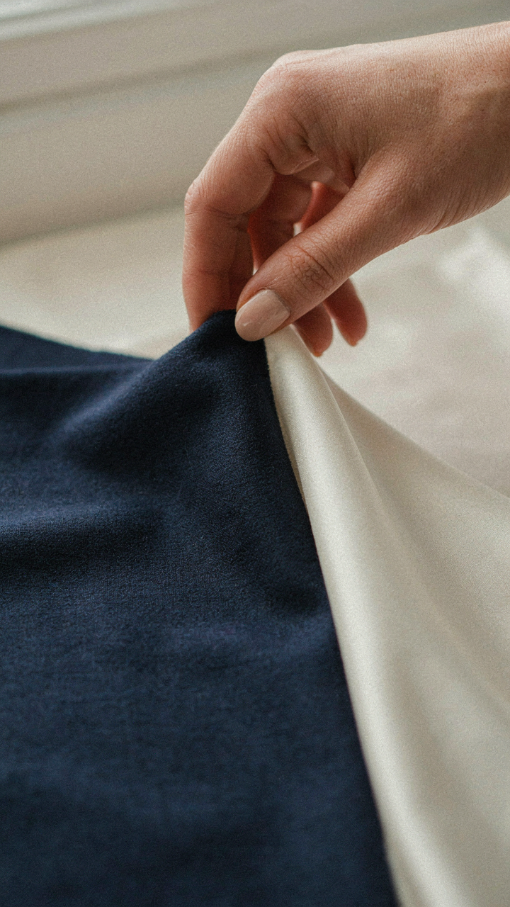 Hand touching luxurious navy wool crepe fabric next to synthetic satin.