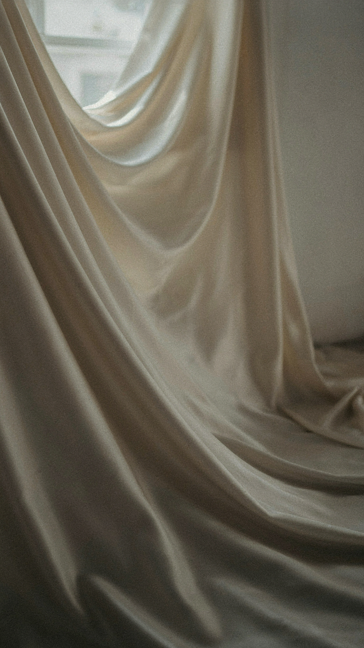 Close-up of ivory satin fabric, elegantly reflecting soft light.