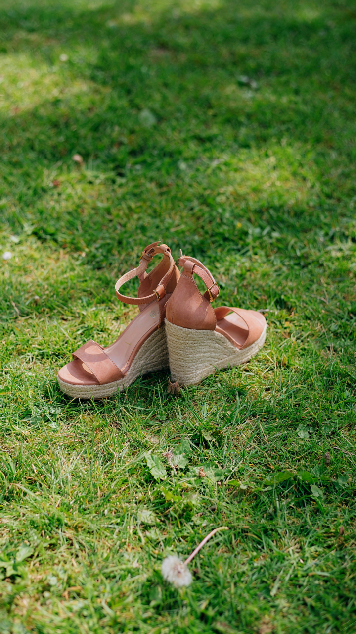 Elegant wedge sandals sit stably on green grass, showing a wide sole.