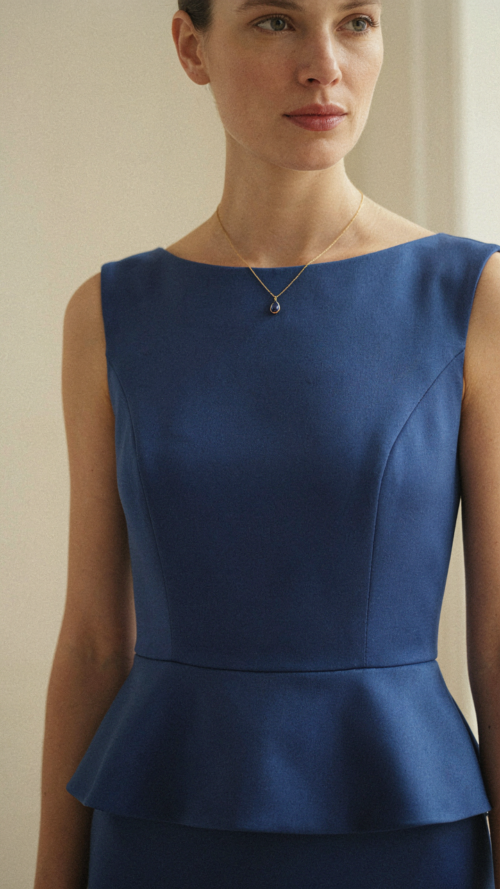 A close-up of a sapphire peplum cocktail dress with a pendant necklace.