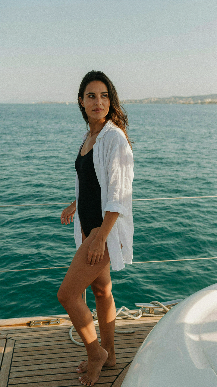 Woman in a fitted swimsuit and sheer linen cover-up on a yacht.