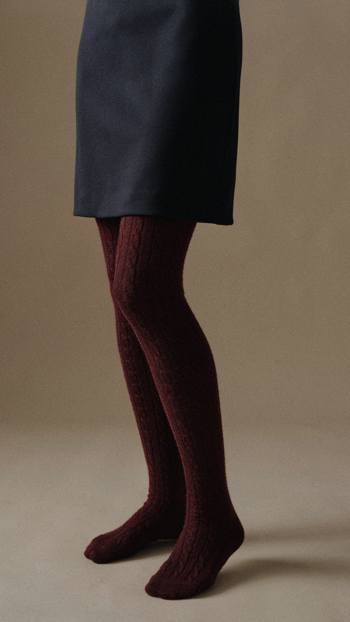 A person's legs in burgundy cable-knit tights with a navy cocktail dress.