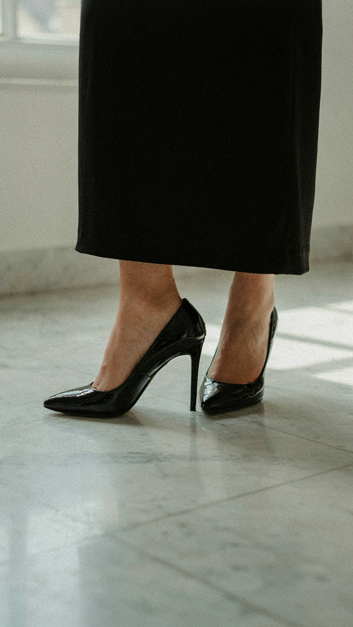 A woman's feet in heels with the hem of a tailored black gown.
