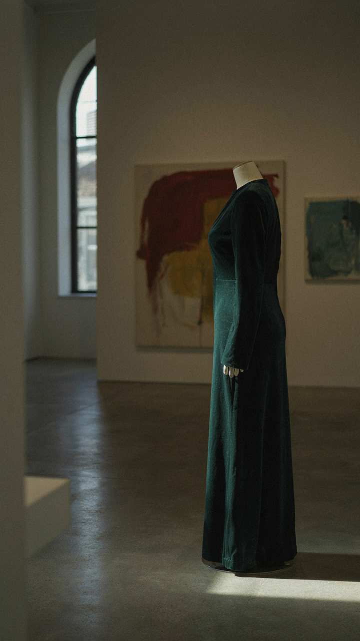 A velvet jumpsuit on a mannequin in a dimly lit art gallery.