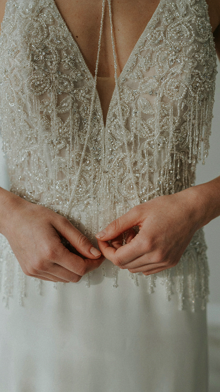 Close-up of hands holding a luxurious beaded halter cocktail dress with fringe.