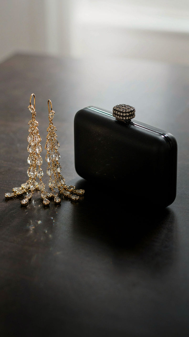 Gold chandelier earrings next to a structured black clutch with a jewel.