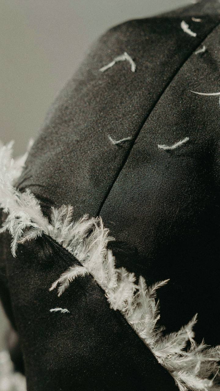 A close-up of white feather trim on dark matte crepe fabric.