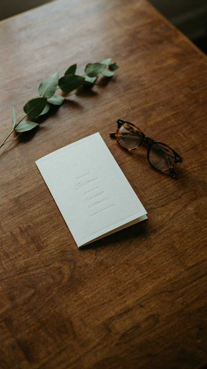 A formal invitation card and reading glasses on a polished table.