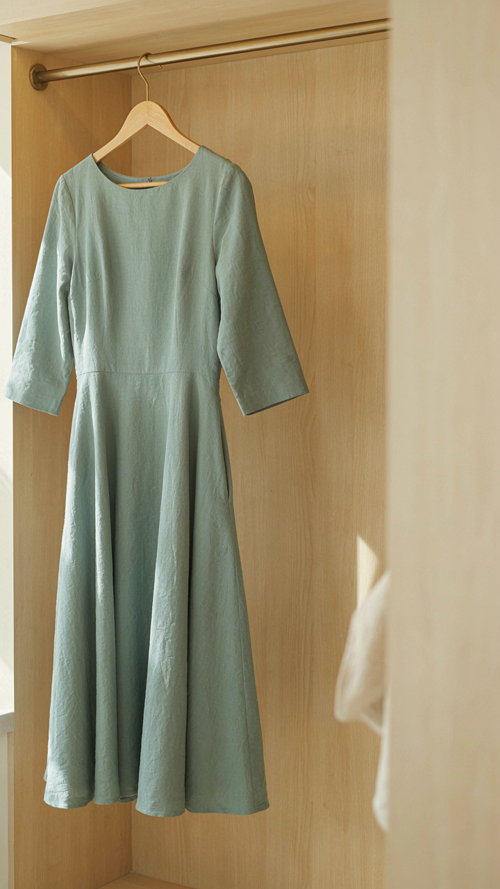 A sage green A-line dress with three-quarter sleeves hangs on a hanger.